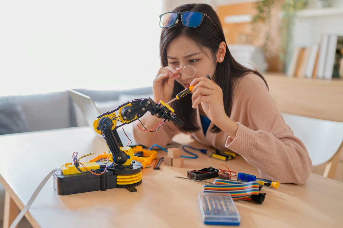 돋보기로 로봇 팔 부품을 들여다보며 드라이버로 조정해 보는 장면