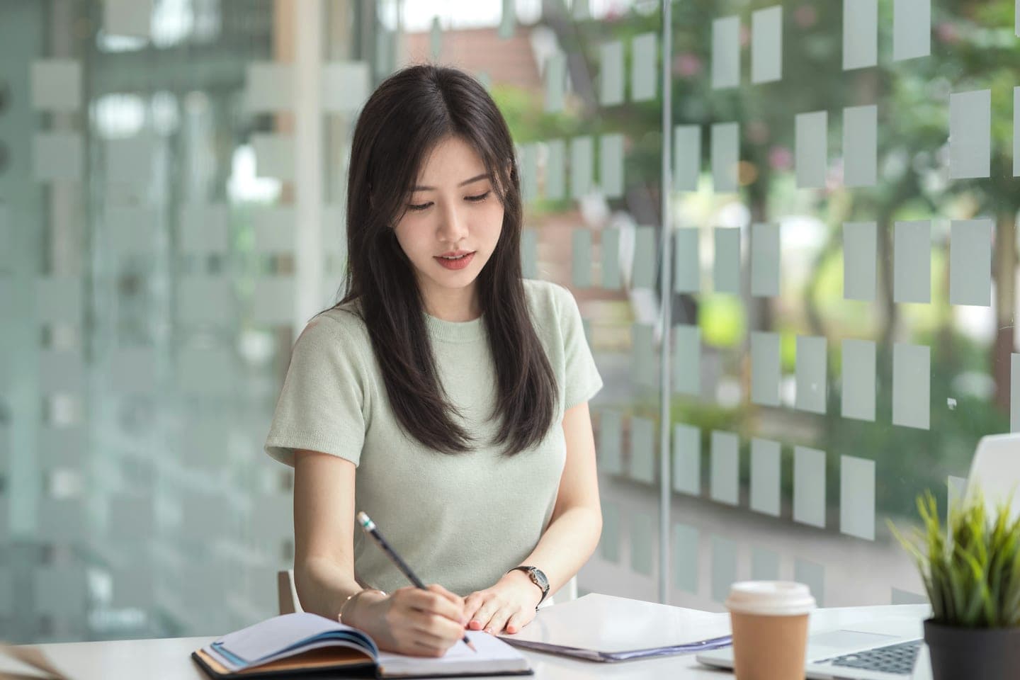 유리벽 옆 흰 책상에서 커피잔을 곁에 두고 공책에 공부 계획을 적는 장면