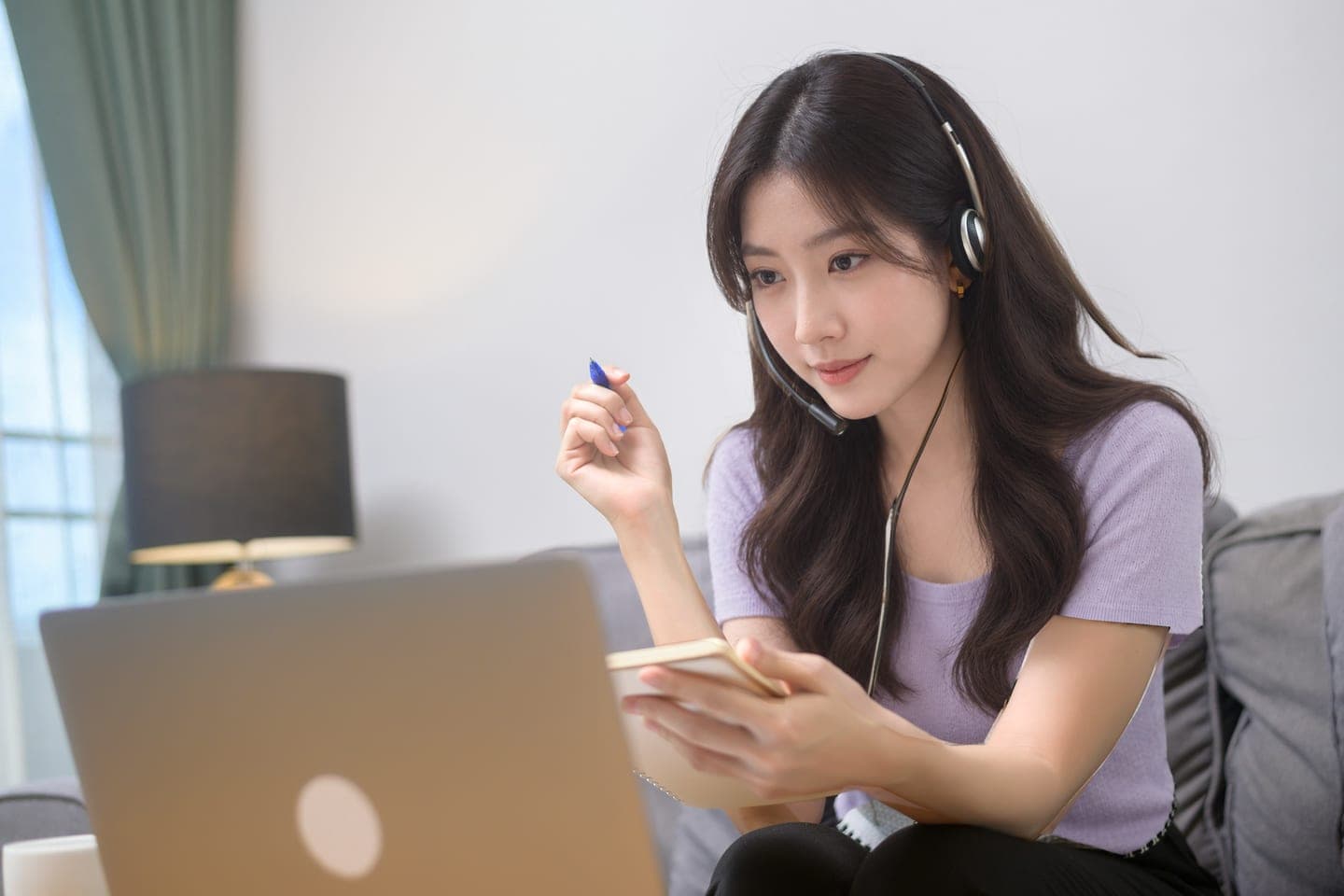 마이크 달린 헤드셋을 쓰고 소파에 앉아 노트북 화면을 보며 작은 수첩에 받아 적는 온라인 수업 장면