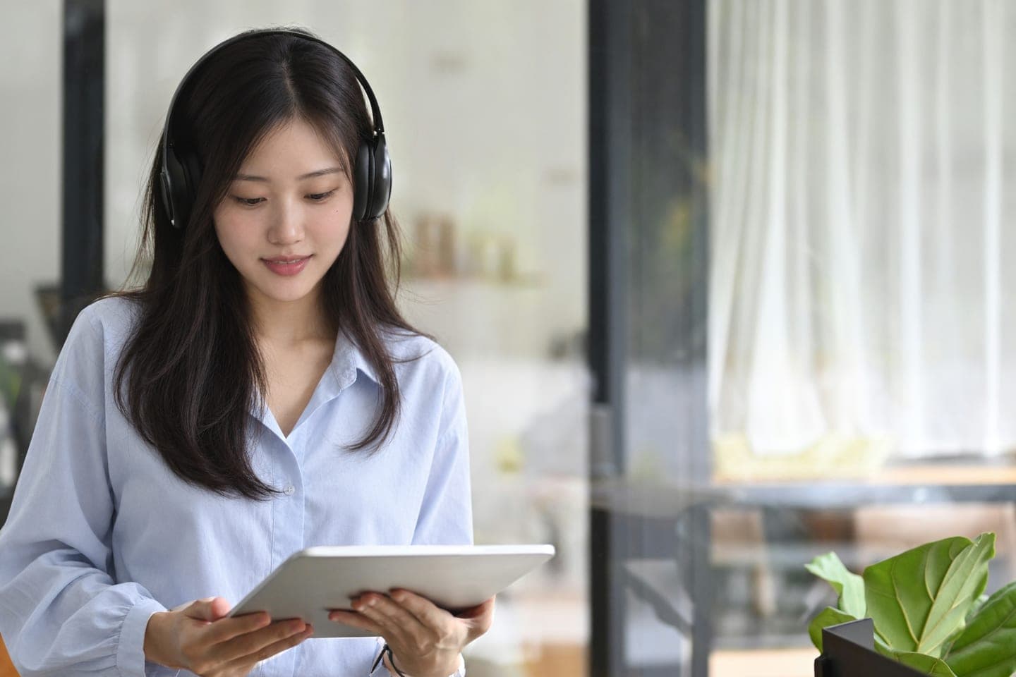 헤드폰을 쓰고 두 손으로 든 태블릿 화면을 보며 수업을 듣는 장면